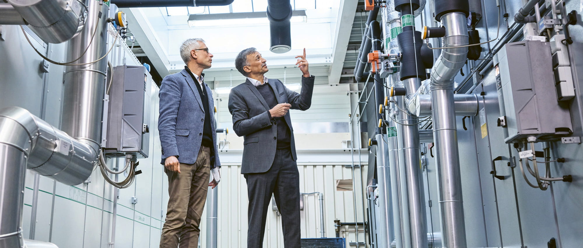 Two men are looking at compressors in a factory.