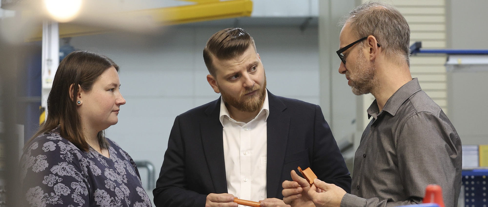 A woman and two men, Kira Truxius, Marco Sutter and Björn Hellbach, hold a piece of Quantix® ULTRA high-performance plastic in their hands and are immersed in a conversation.