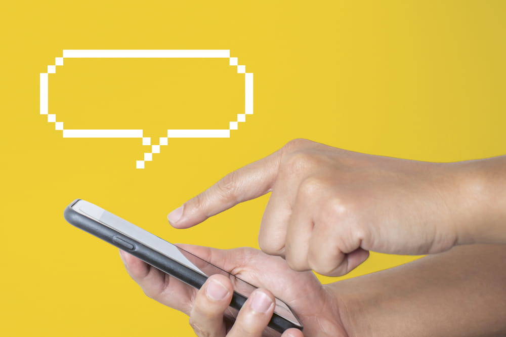 A hand is touching a phone. In the yellow background pops up a speech bubble. Copyright: iStock/Phira Phonruewiangphing