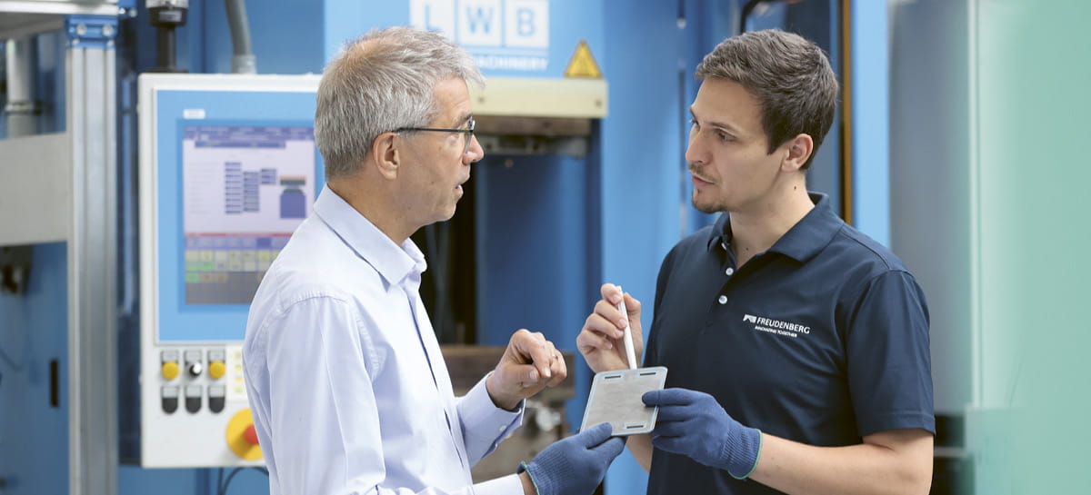 Two man stand in a factory and have a conversation.