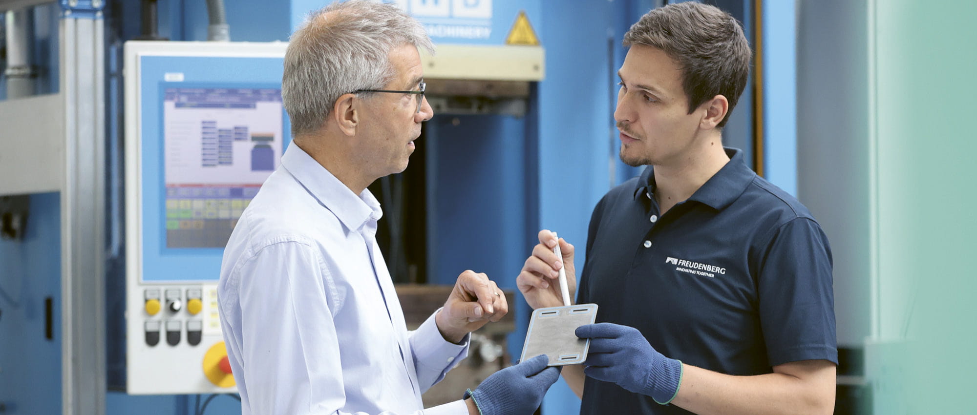 Two man stand in a factory and have a conversation.