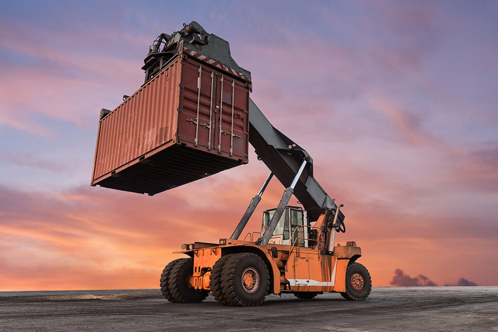 Heavy-duty lift truck hoisting a shipping container at sunset.