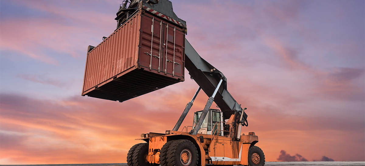 Heavy-duty lift truck hoisting a shipping container at sunset.